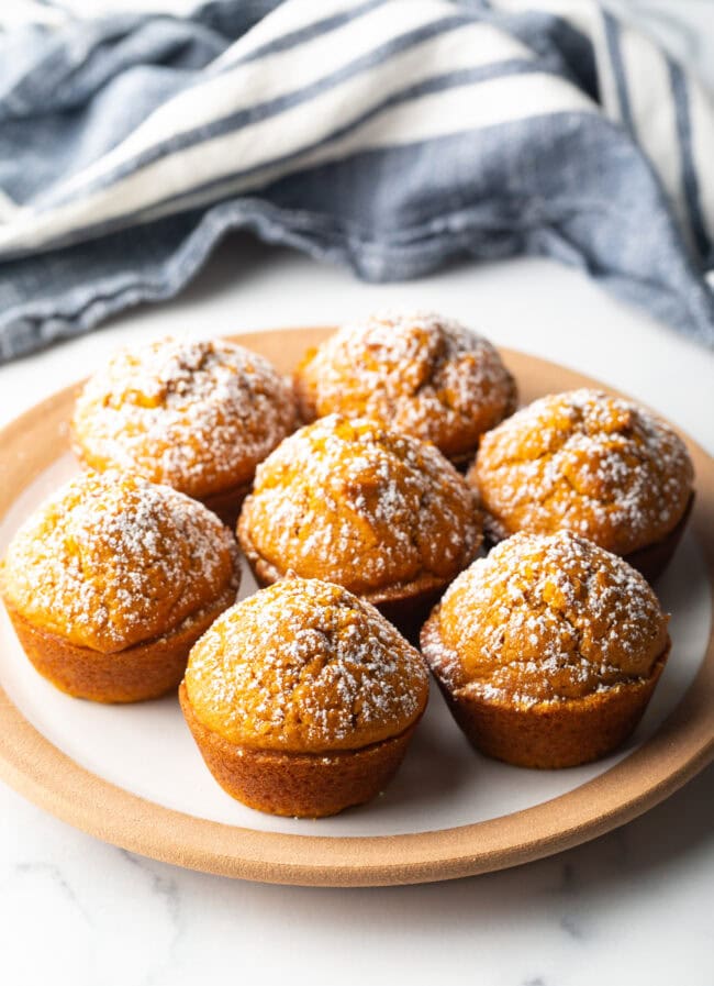 7 pumpkin muffins dusted with powdered sugar, arranged on a plate.