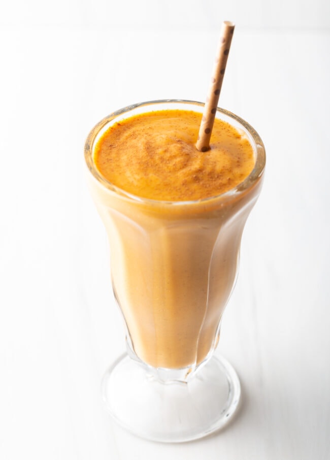 Milkshake glass with pumpkin pie smoothie and straw.