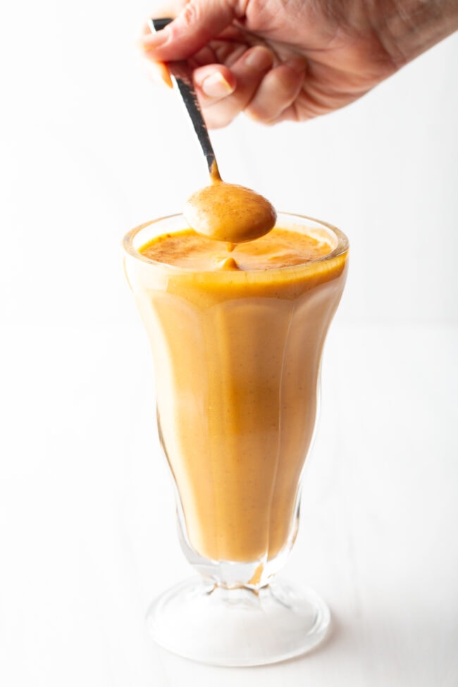 Milkshake glass, with a hand holding metal spoon showing a spoonful of protein shake to camera