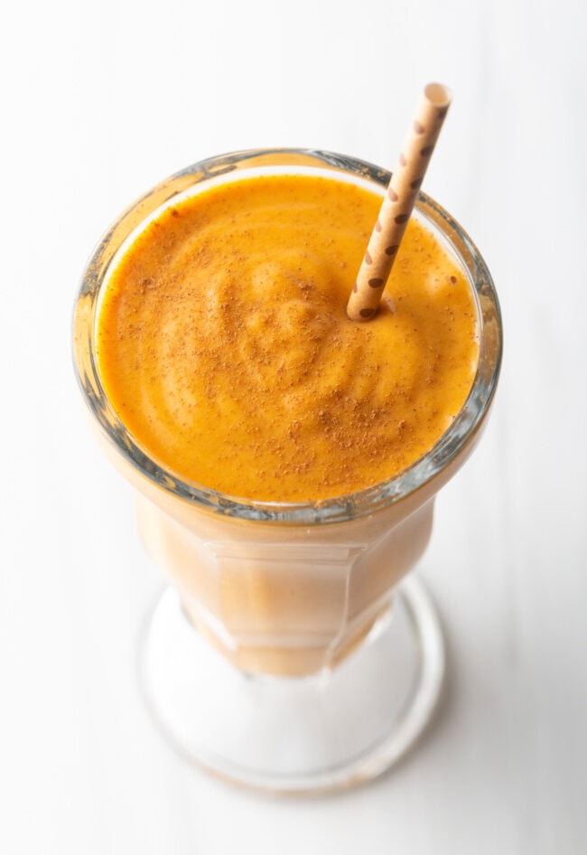 Milkshake glass with pumpkin pie smoothie and straw.