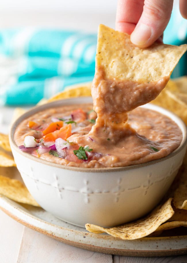 Hand dipping a tortilla chip into bean dip. 