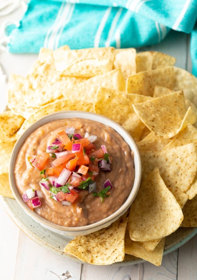 Pinto bean dip served in a bowl with pico de gallo on top next to a plate of tortilla chips. 