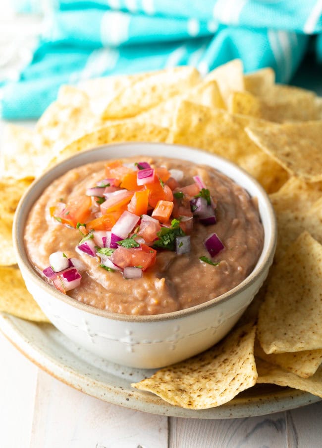 Bean dip served in a white bowl next to chips. 