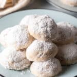 Light blue plate stacked with 3 layers of white Russian tea cakes covered in powdered sugar.