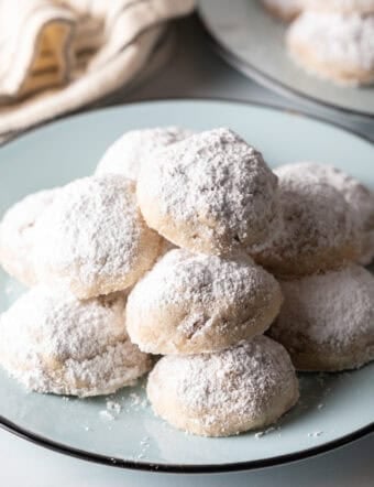 Light blue plate stacked with 3 layers of white Russian tea cakes covered in powdered sugar.