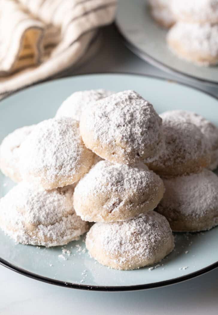 Light blue plate stacked with 3 layers of white Russian tea cakes covered in powdered sugar.