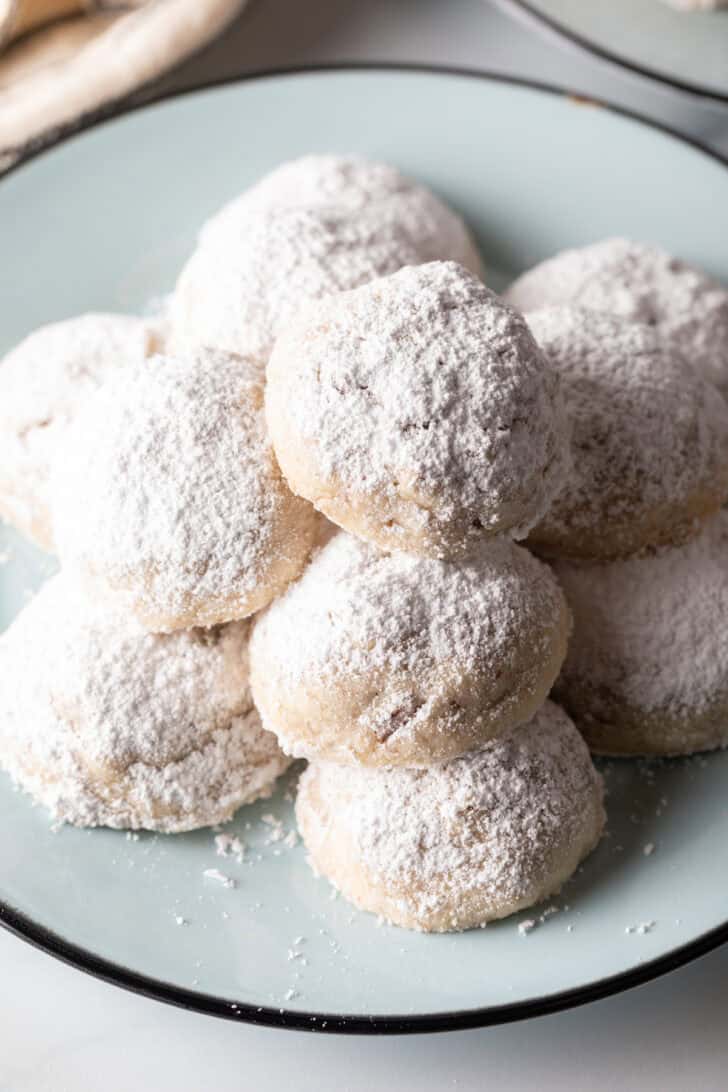 Light blue plate stacked with 3 layers of white Russian tea cakes covered in powdered sugar.