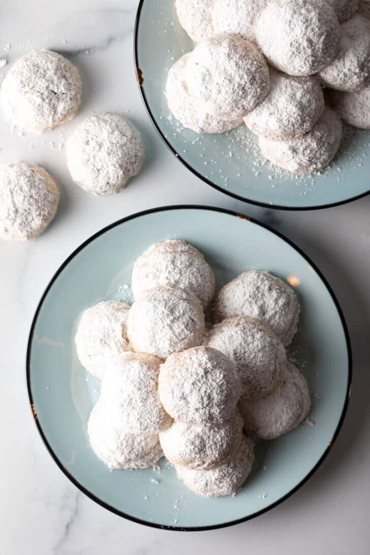 Light blue plate stacked with 3 layers of white Russian tea cakes covered in powdered sugar.