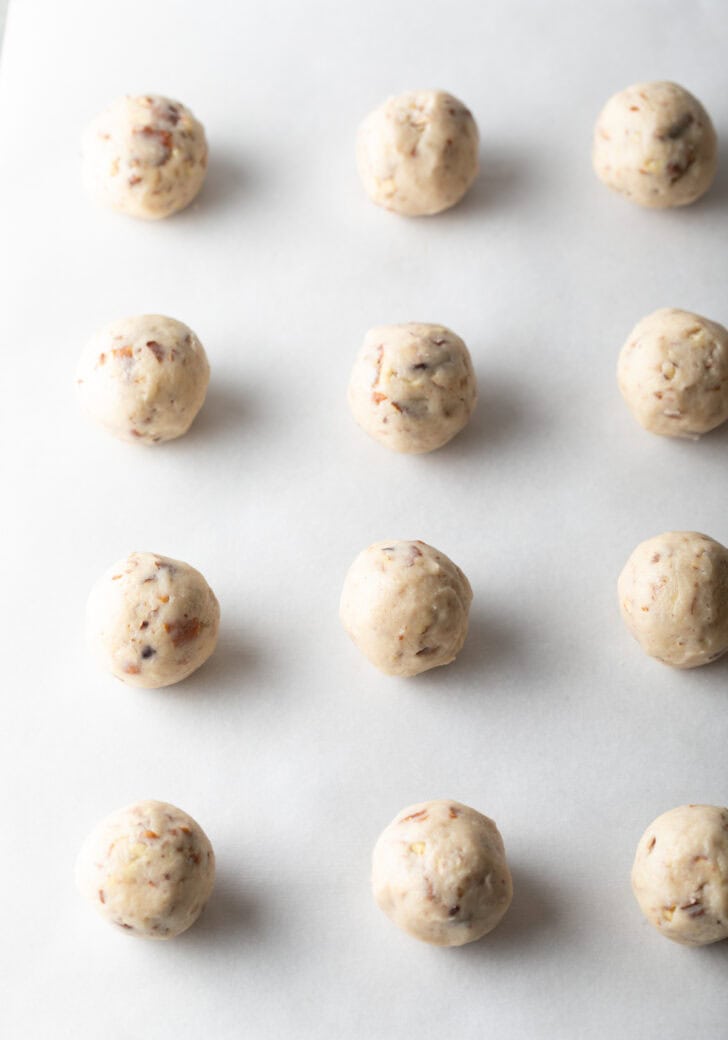 A dozen round balls of cookie dough on a baking sheet.