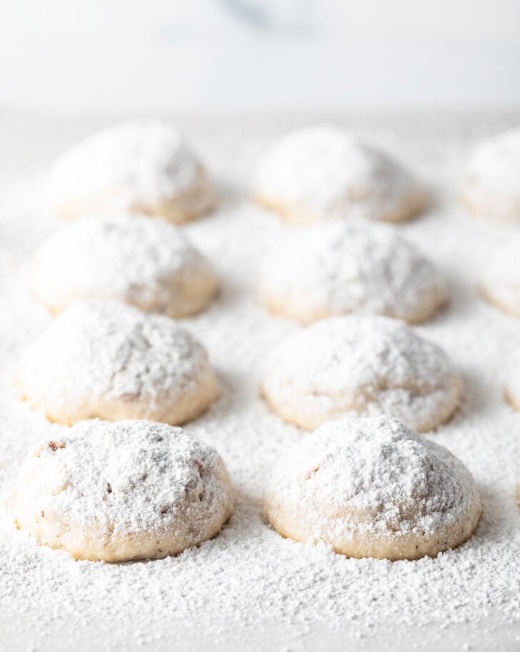 8 snowball cookies on a baking sheet, covered with a heavy layer of powdered sugar.