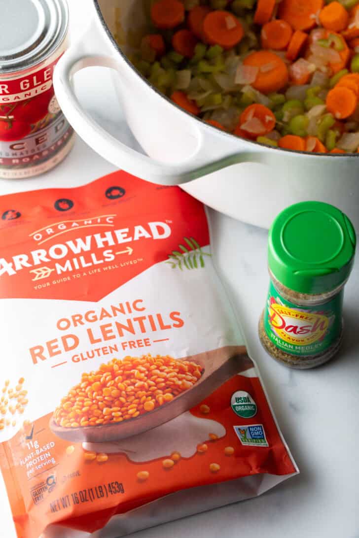 Bag of red lentils, a jar of seasonings, a cooking pot with sliced carrots.