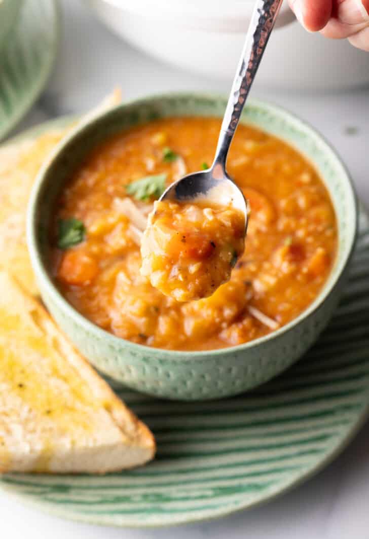 A hand is holding a spoonful of soup to camera.