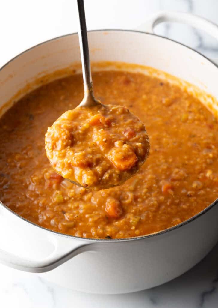 Large cooking pot with lentil and carrot soup. A ladleful is showing to camera.