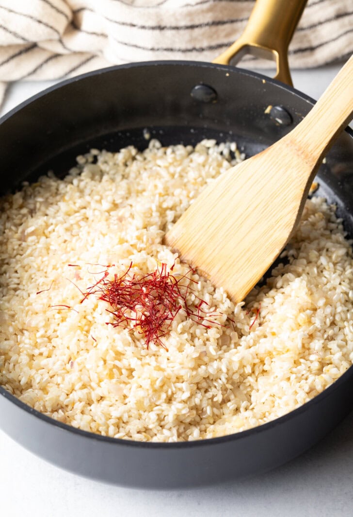 Wooden spatula stirring saffron and rice in a deep skillet.