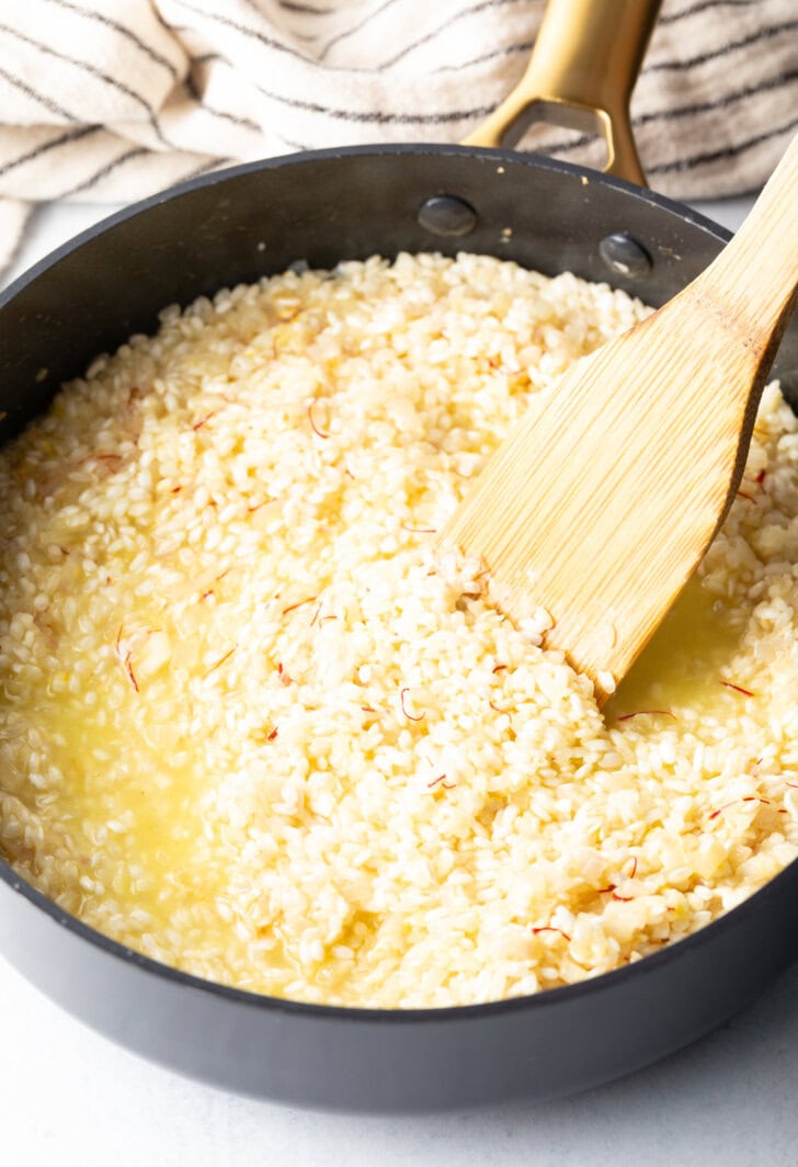 Wooden spatula stirring rice in a large deep skillet.