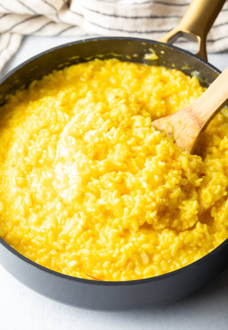 Wooden spatula stirring yellow risotto in a large deep skillet.