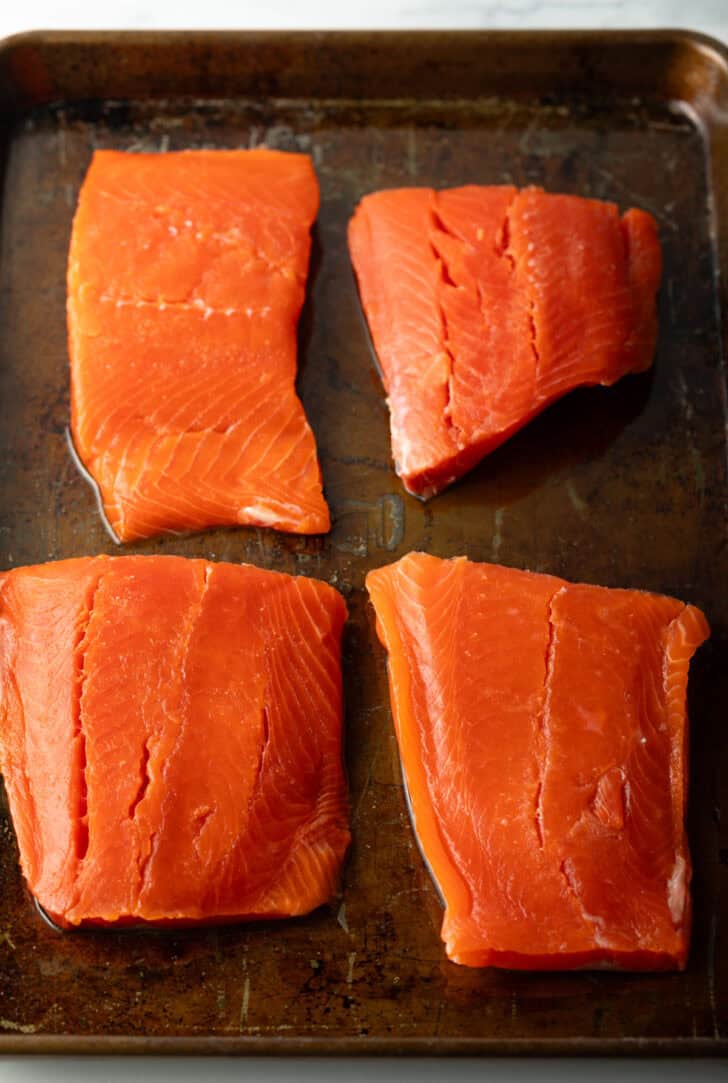 4 raw pieces of salmon filets on a baking sheet.