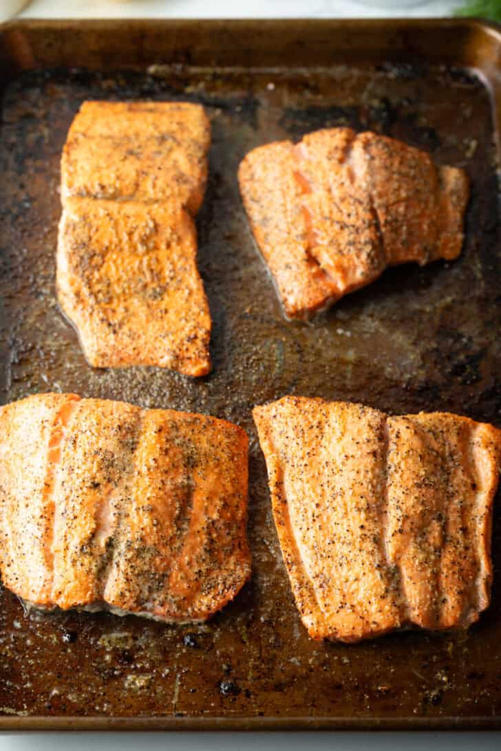 4 baked seasoned filets of salmon on a baking sheet.