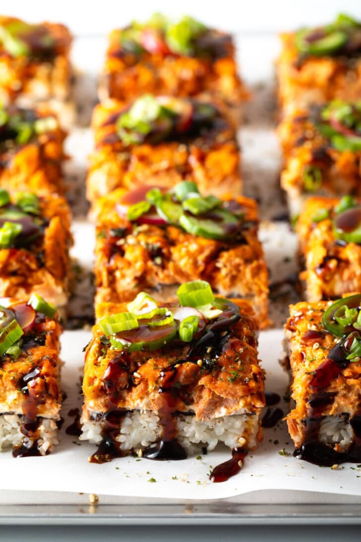 Rows of square slices of sushi bake on a baking sheet.