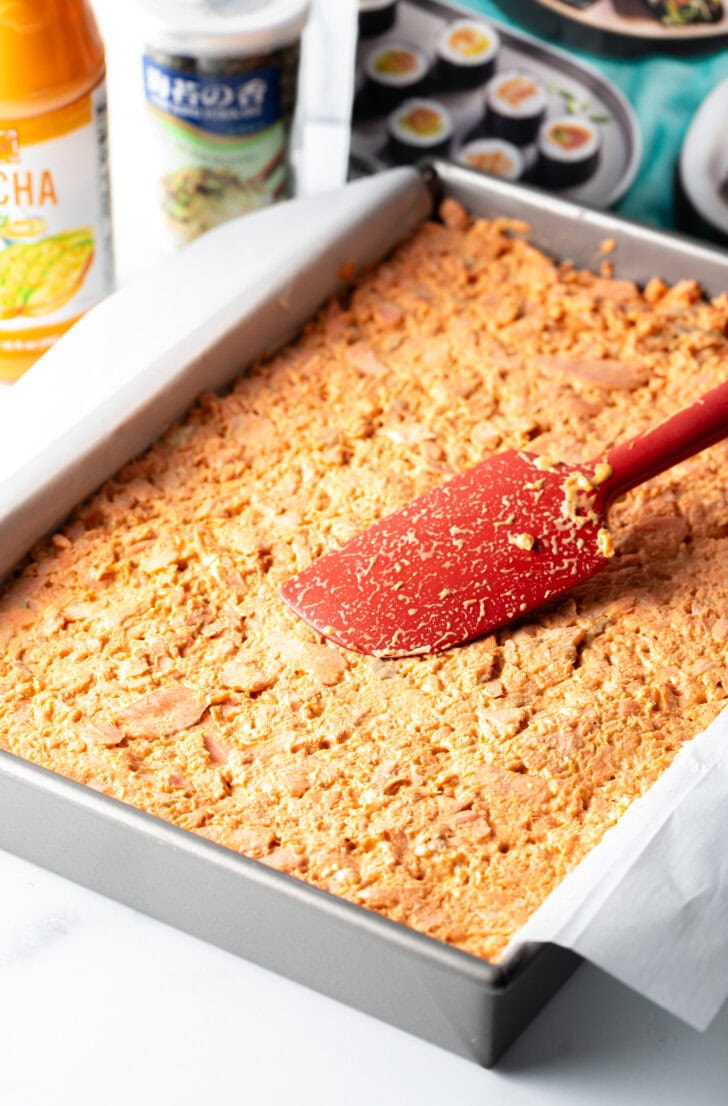 Red spatula smoothing salmon mixture into a baking pan.