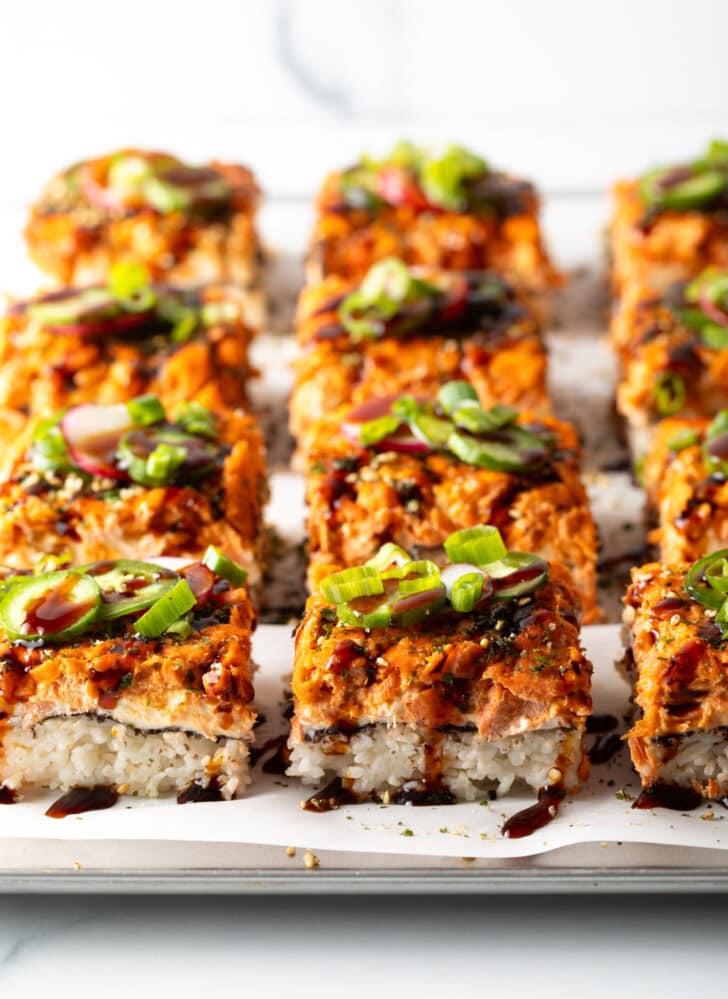 Rows of square slices of sushi bake on a baking sheet.