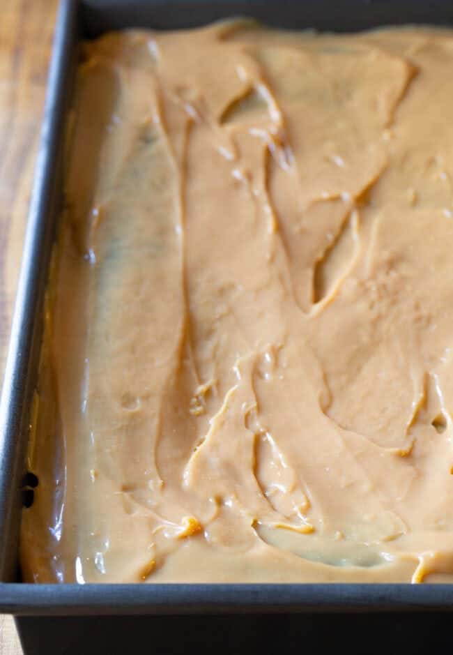 A baking sheet sits on top of a kitchen counter containing a baked chocolate cake covered with caramel sauce. 