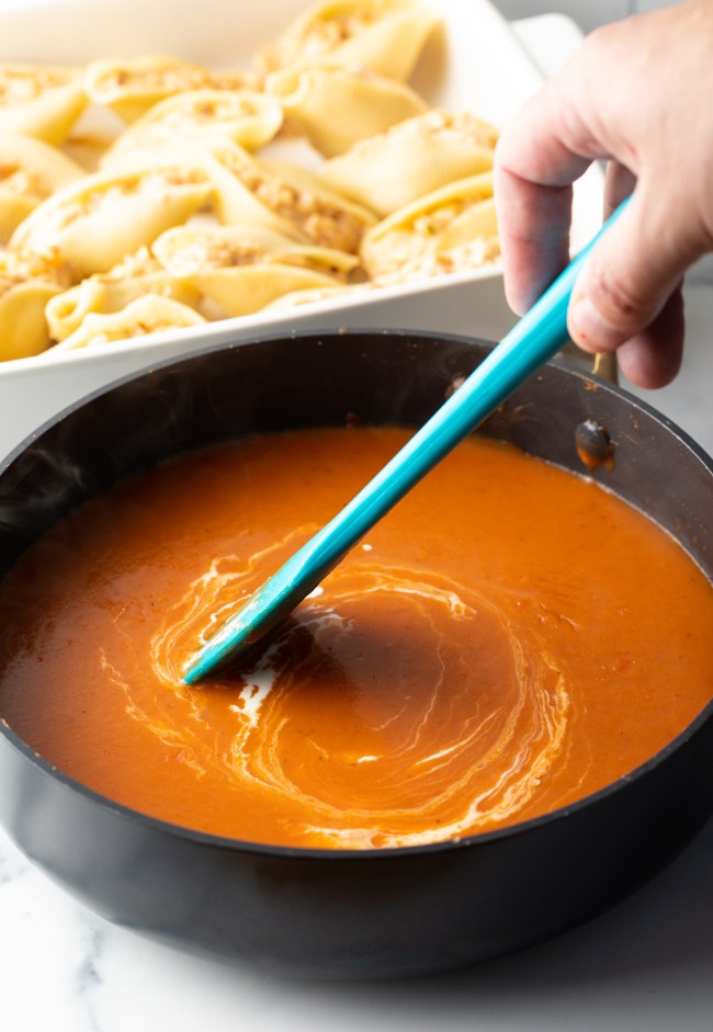 Hand with blue spatula stirring cheese mixture in a saucepan.