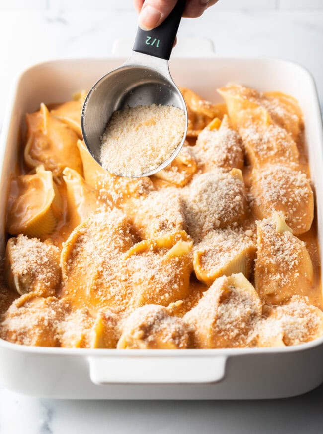 Adding grated parmesan cheese to the baking dish with stuffed pasta.