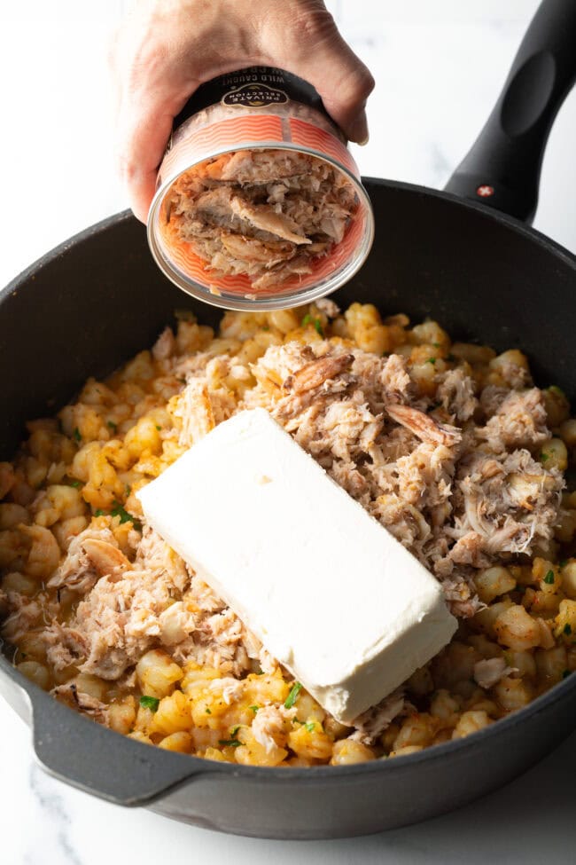 Adding cream cheese and water to the skillet with seafood.