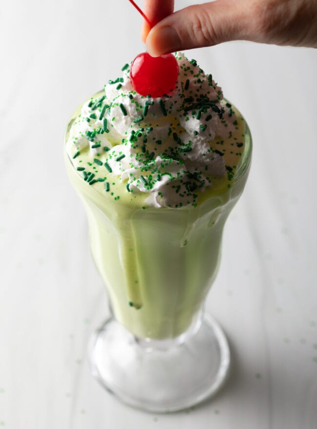 Peppermint shamrock shake in a glass, with cherry on top.