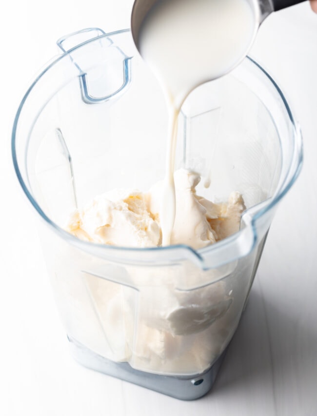 Pouring milk over ice cream in a blender jar.