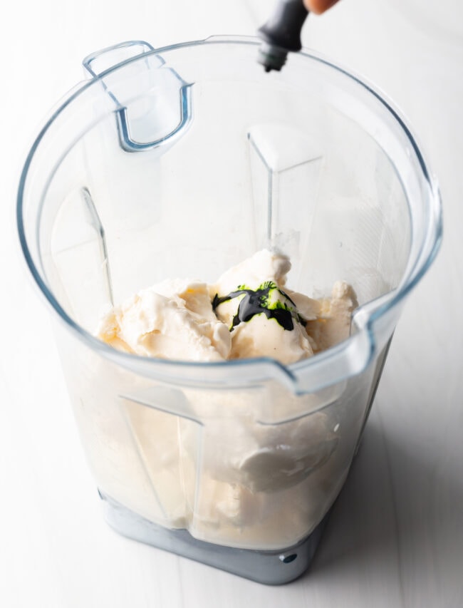 Ice cream and drizzle of green food coloring in a blender jar.