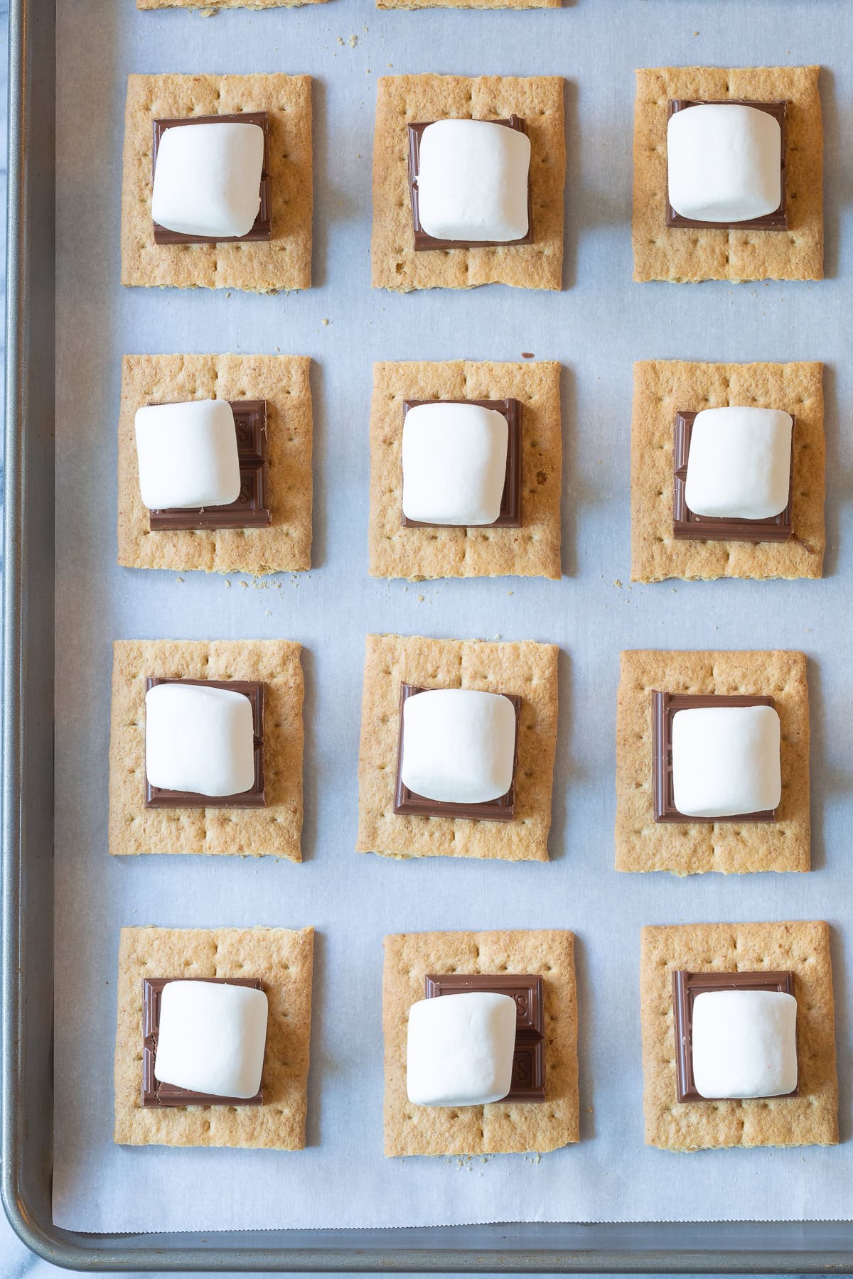 Overhead shot of graham crackers topped with chocolate and marshmallows before being broiled. 