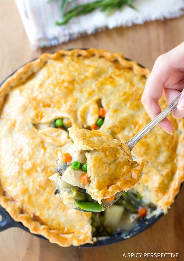 Turkey pot pie with a spoon above it with a large bite of the pot pie. 