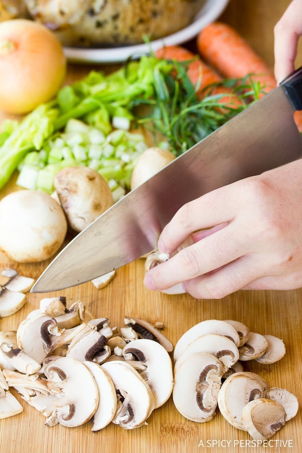 Hands holding a large chef's knife and slicing mushrooms on a cutting board. 