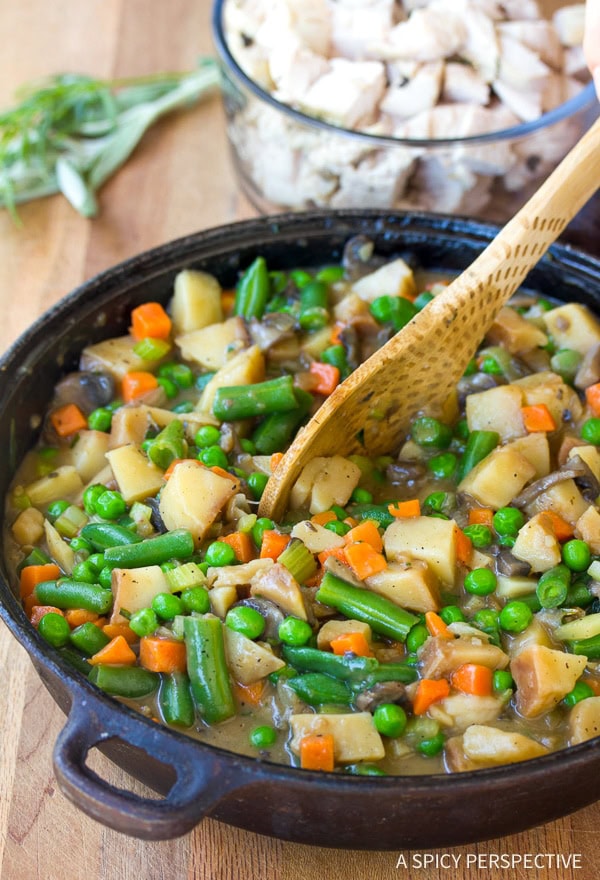 Turkey pot pie filling in a skillet being stirred with a wooden spoon. 