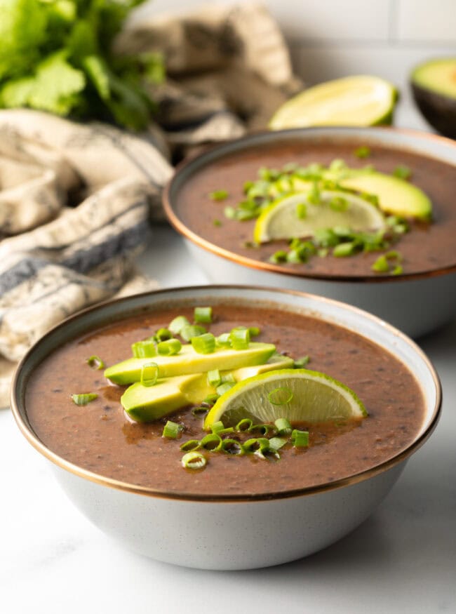 crock pot black bean soup with avocado, scallions, and lime on top