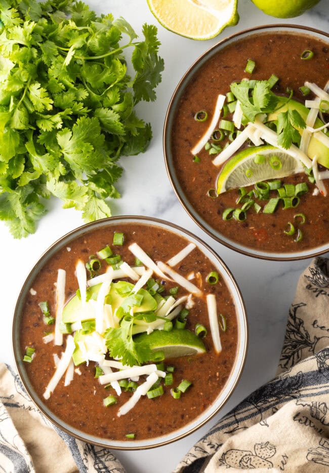 overhead shots of black bean soup crock pot - cheese, limes, and cilantro on top