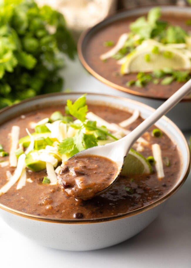 crock pot black bean soup spooned up from gray bowl