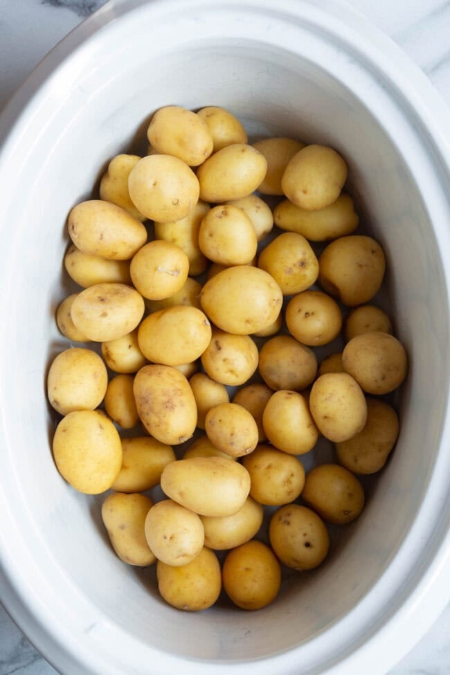 Raw potatoes in a white slow cooker. 