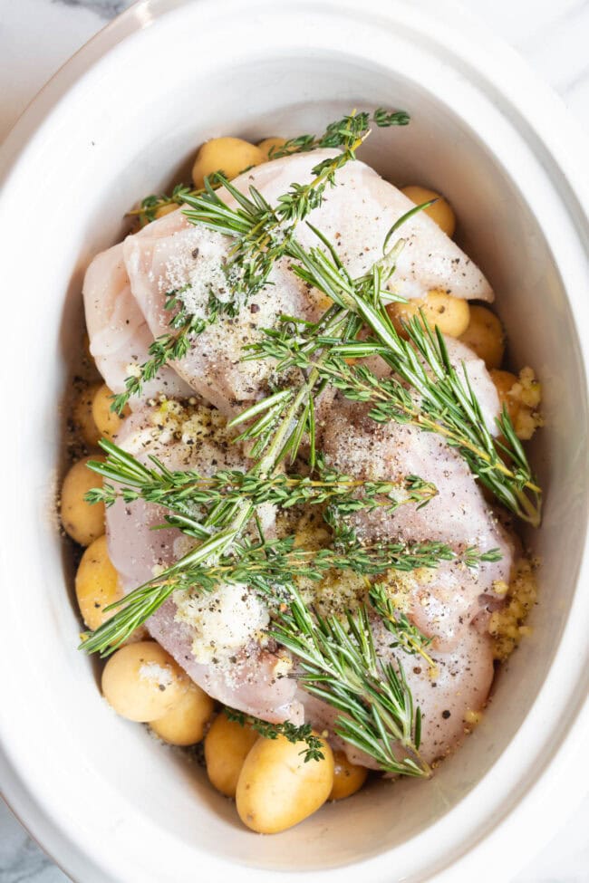 Garlic butter chicken with fresh herbs in a crockpot before being cooked. 