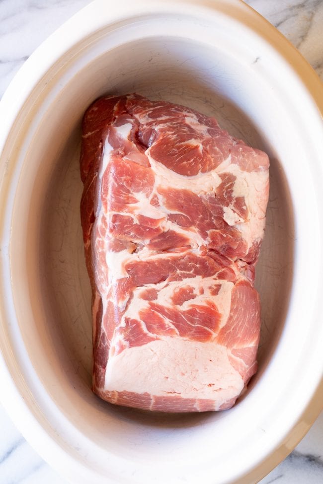 Pork butt roast in a white crockpot.