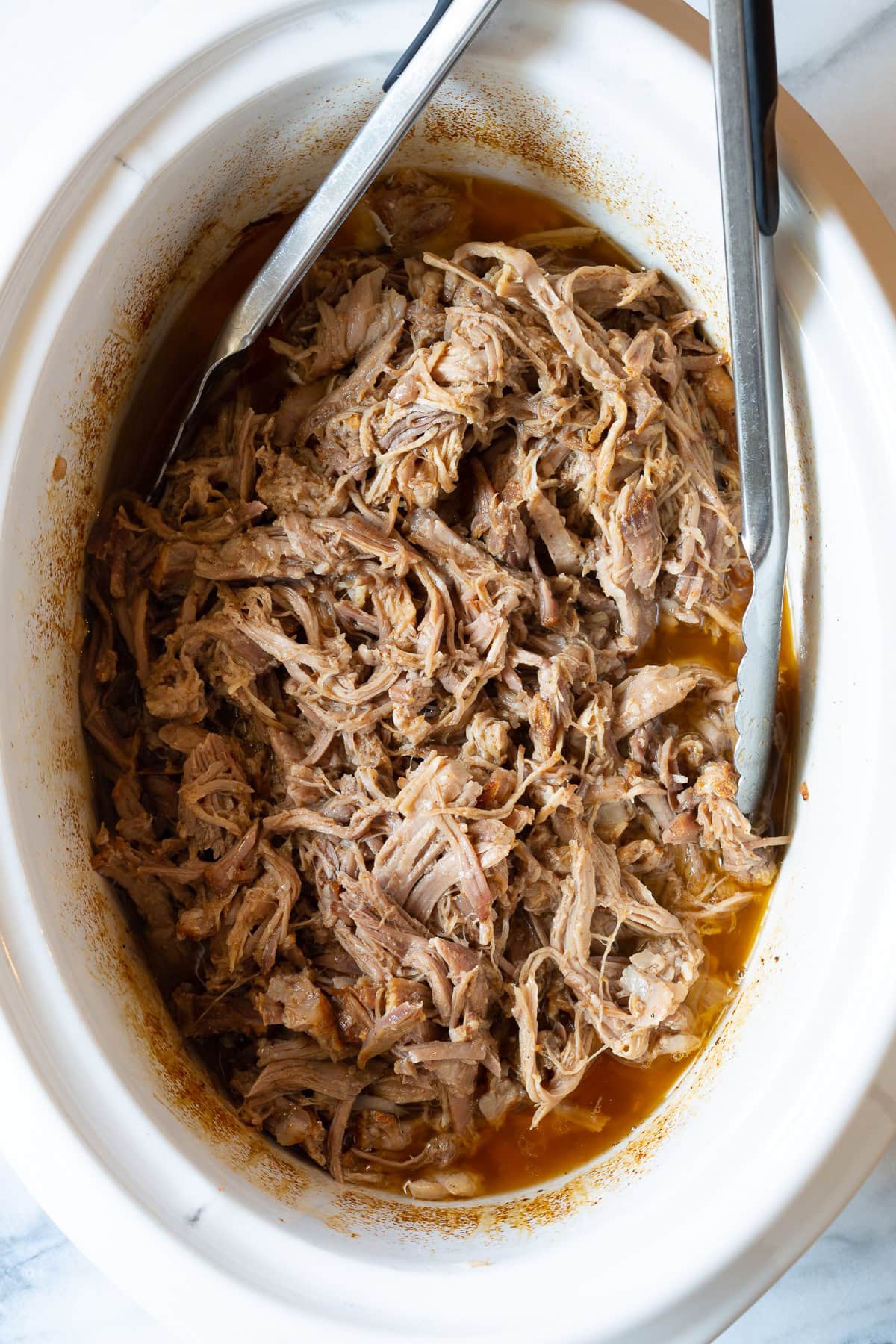 shredded pork in the crockpot with metal tongs