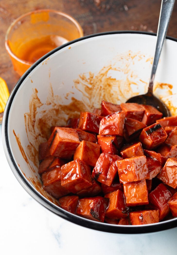 Spoon tossing cubes of smoked baloney in a white bowl.