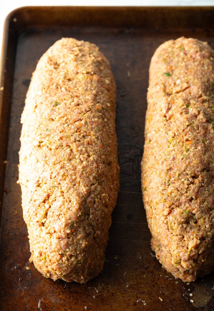 Two raw meatloafs laying side-by-side on a baking sheet.