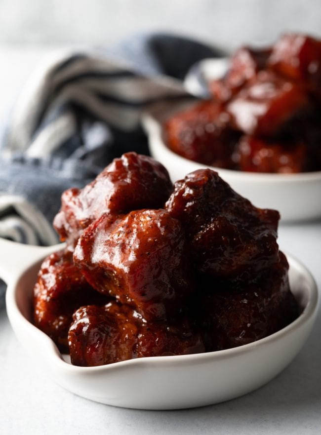 Close view bowl overloaded with bites of smoked pork belly burnt ends in bbq sauce.