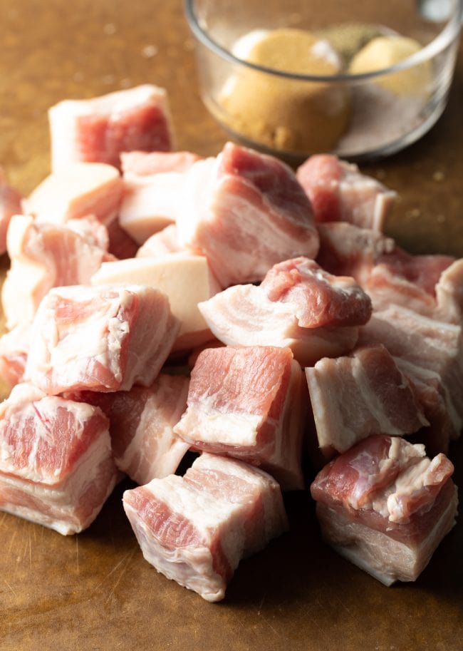 Raw cubes of pork belly on a cutting board.