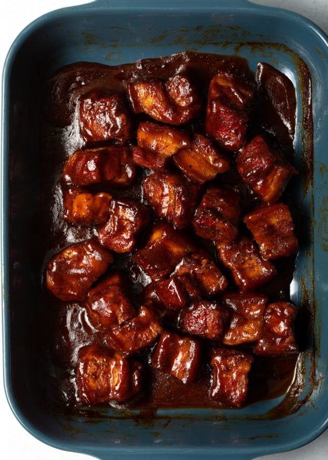 Top down smoked pork belly coated in bbq sauce in a baking dish.