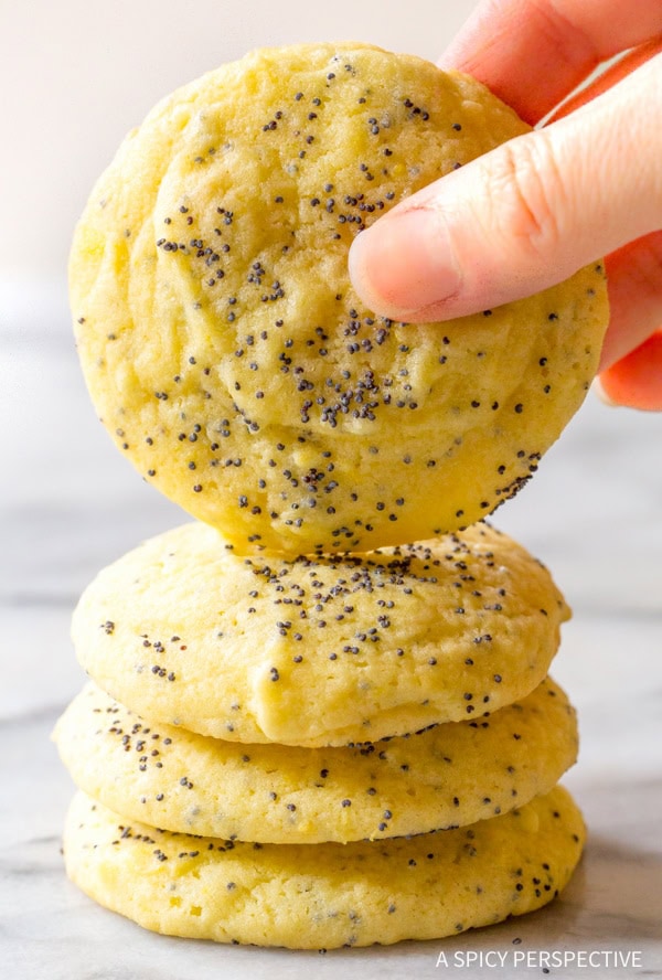 Hand holding a lemon poppy seed cookie recipe with more cookies stacked underneath. 