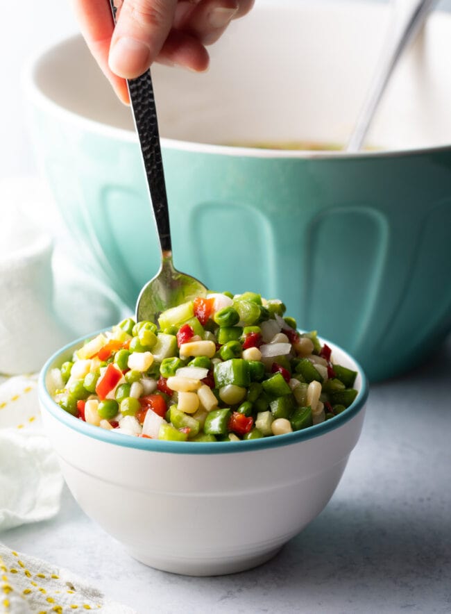 Marinated Vegetable Salad Recipe - Finished shoepeg corn, pea, and marinated veggies salad. Metal spoon is in the white bowl.